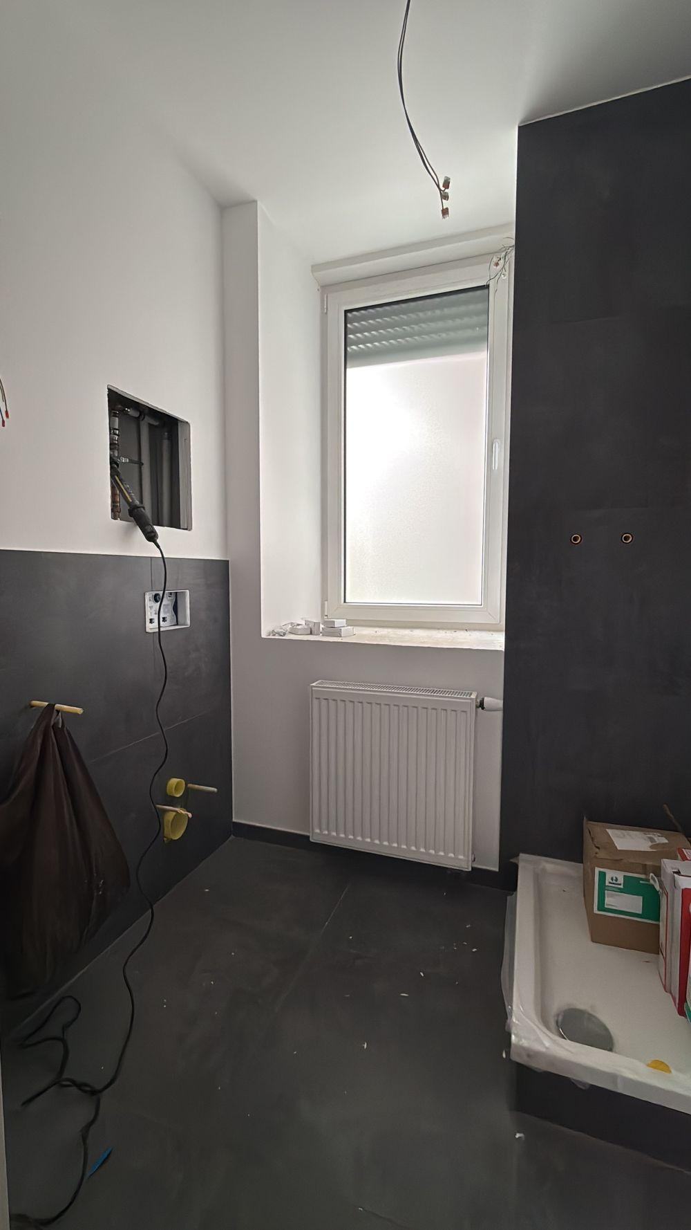 Badezimmer mit Fenster, Heizkörper, dunklen Wandfliesen und vorbereiteter Duschtasse