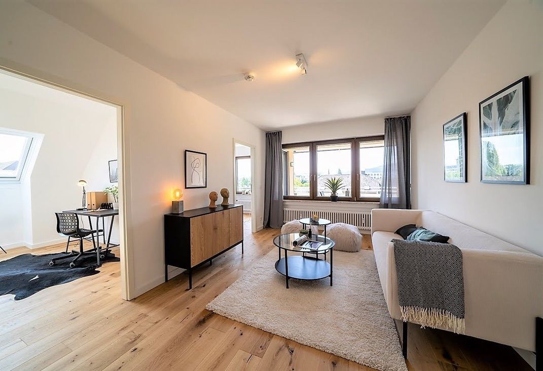 Heller Wohnraum mit Eichenholzboden, hellem Sofa, Sideboard und großem Fenster mit Blick über Trier