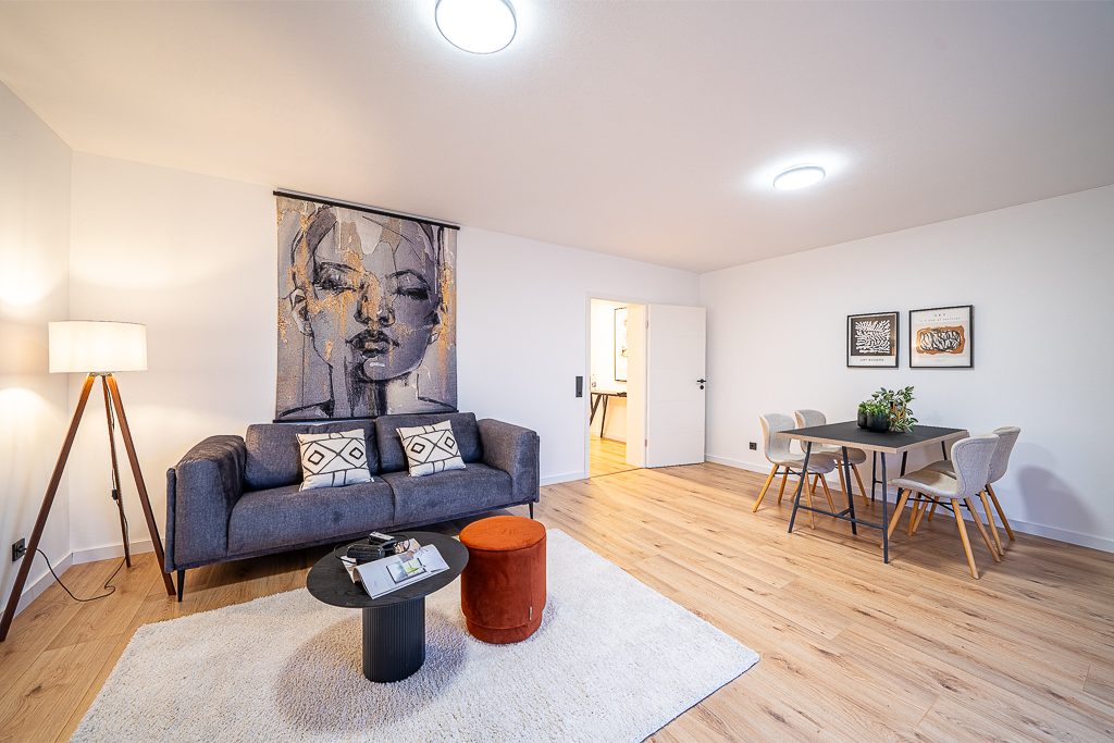 Wohnzimmer mit Esstisch, Stühlen, dunklem Sofa und Balkontür