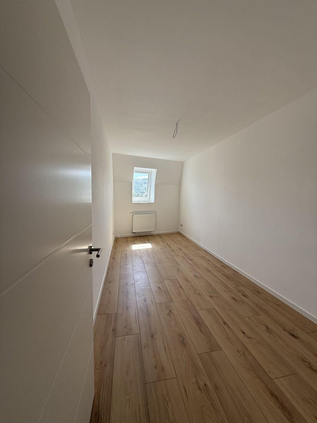 Leeres Zimmer mit Dachschräge, Gaubenfenster, Heizkörper und hellem Boden in Eichenoptik