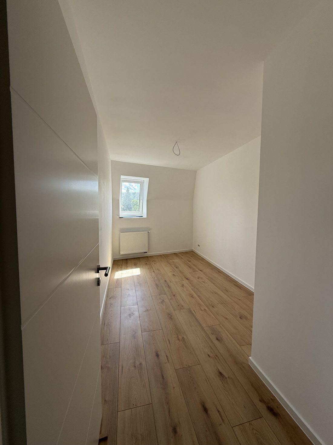 Weiteres leeres Zimmer mit Dachschräge, Gaubenfenster und Heizkörper unter dem Fenster
